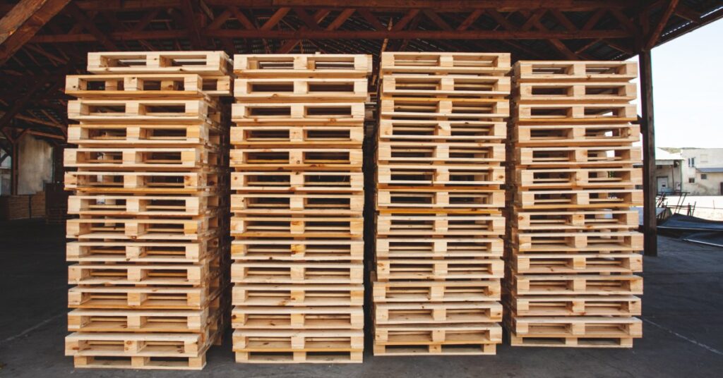 Four tall stacks of pallets in a covered outdoor storage area. Each column has a small gap between them.