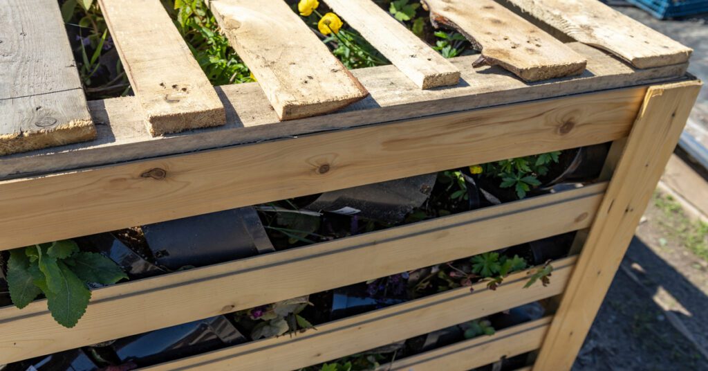A wooden box with interior shelves made out of repurposed pallets. The shelves feature a range of small potted plants.